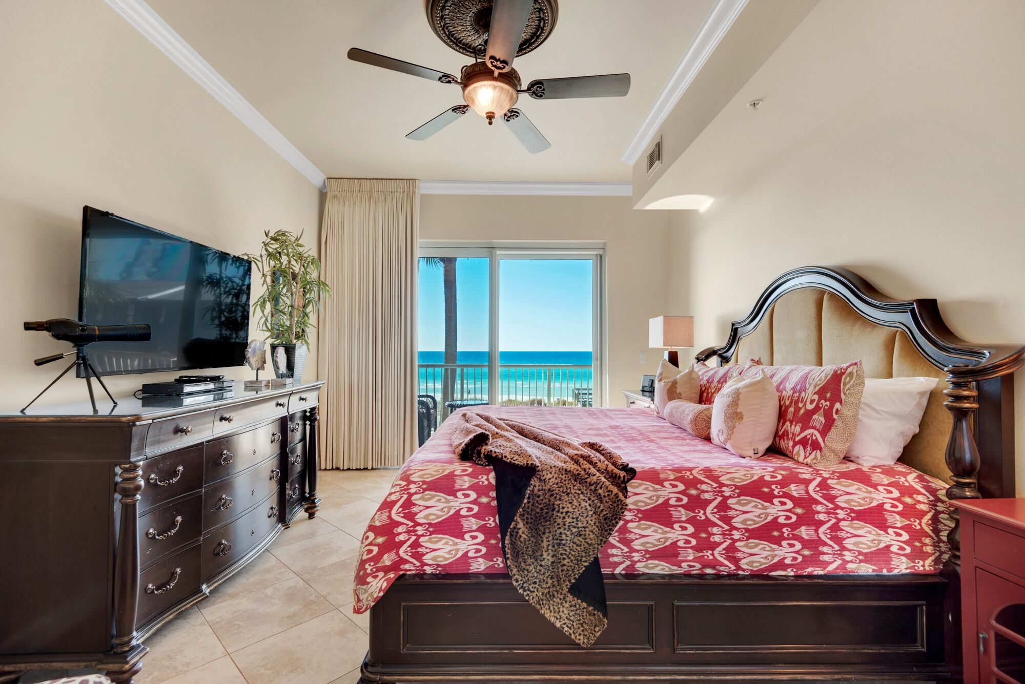 A hotel room with a large bed, a television, a dresser, and a balcony with a view of the ocean.