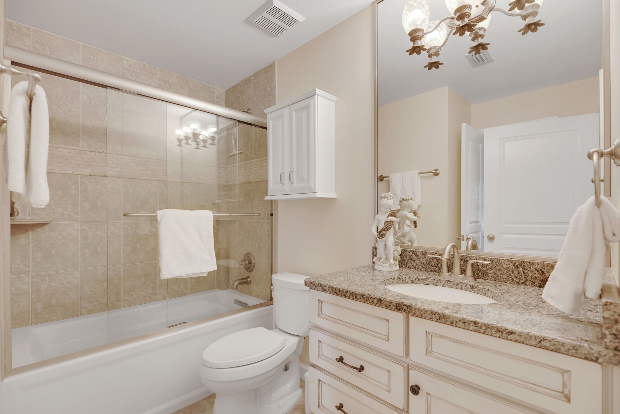A bathroom with a glass-enclosed shower, a toilet, a sink with a marble countertop, and a cabinet above the sink.