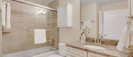 A bathroom with a glass-enclosed shower, a toilet, a sink with a marble countertop, and a cabinet above the sink.