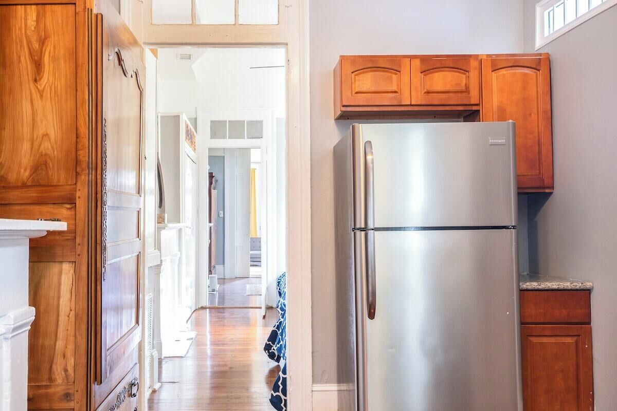 A kitchen with wooden cabinets, a stainless steel refrigerator, and a hallway leading to other rooms.