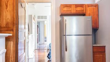 A kitchen with wooden cabinets, a stainless steel refrigerator, and a hallway leading to other rooms.