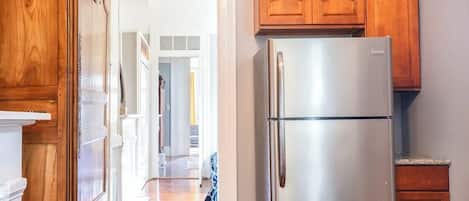 A kitchen with wooden cabinets, a stainless steel refrigerator, and a hallway leading to other rooms.