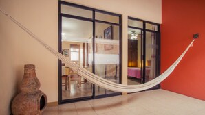A hammock in a room with a large clay pot and a sliding glass door leading to another room.