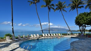 A pool with lounge chairs and palm trees, overlooking a body of water. - Beautiful 2 Bdrm Oceanfront Kihei Condo!  (Kihei)