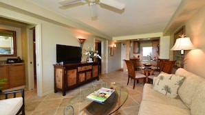 A living room with a glass coffee table, a sofa, a TV, and a ceiling fan. - Beautiful 2 Bdrm Oceanfront Kihei Condo!  (Kihei)