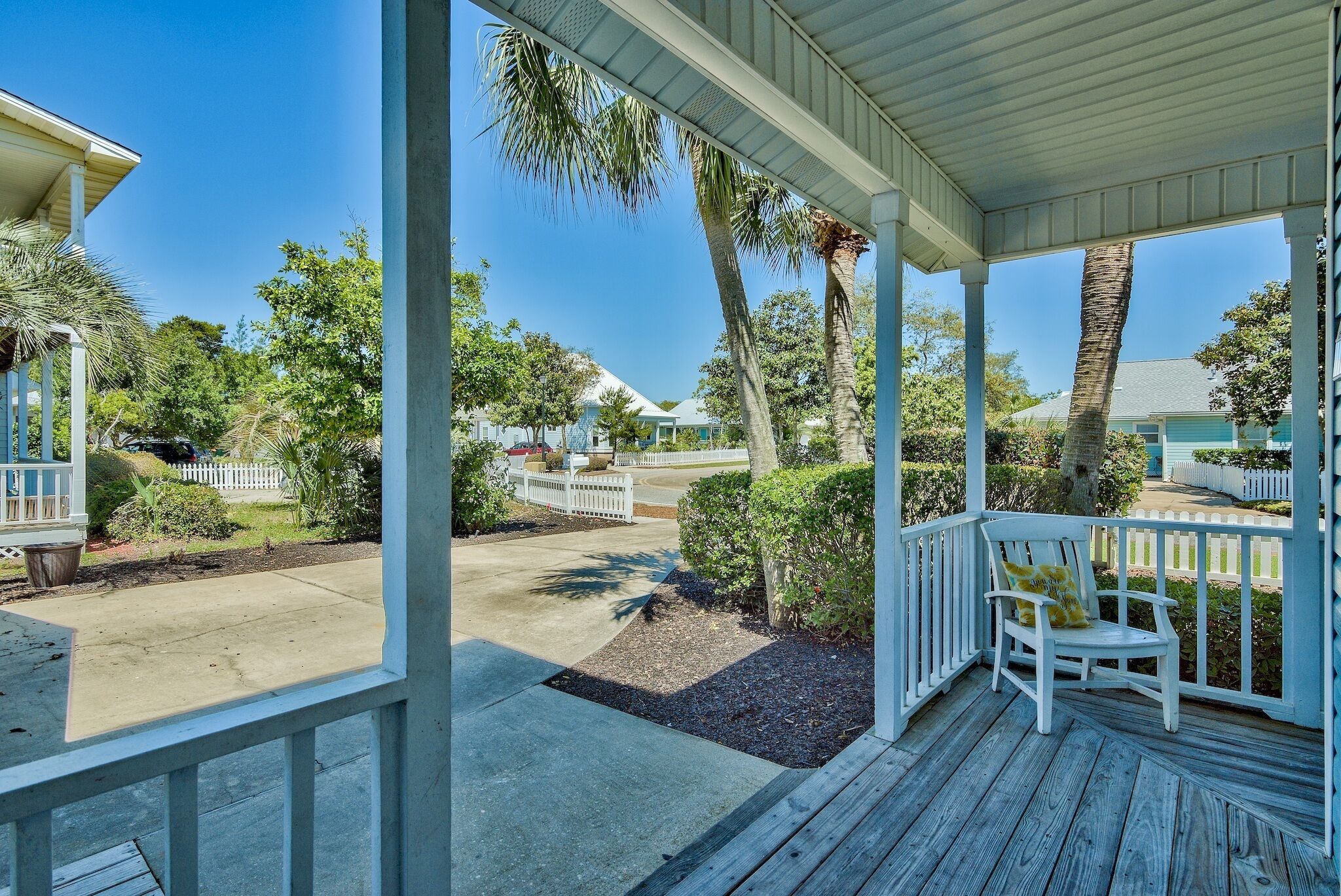 A covered porch with a white chair, a white picket fence, and a clear view of a residential street.