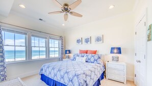 A bedroom with a bed, a nightstand, a lamp, and a ceiling fan. There are windows with a view of the ocean. - Oceanfront Condo w/ Private Sundeck, Resort Pool, Elevator, and Beach Access (Rodanthe)