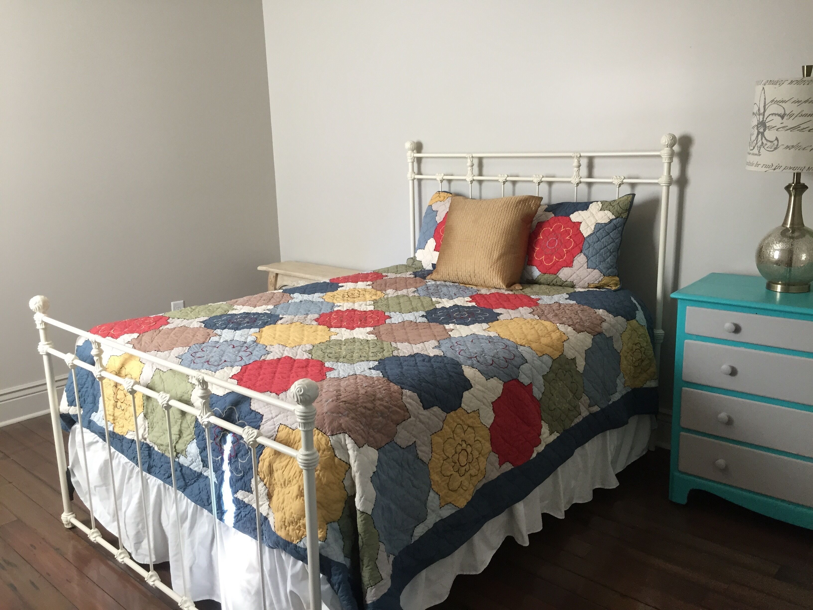 A bed with a colorful quilt, a wooden nightstand, and a teal dresser with drawers.