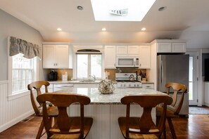 Una cocina moderna con armarios blancos, una isla central con sillas, microondas, estufa y refrigerador.
