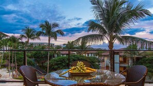 Un balcon avec des fauteuils en osier, une table en verre et une assiette de bananes.