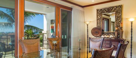 A dining area with a glass table and wicker chairs, a ceiling fan, and a large mirror on the wall.