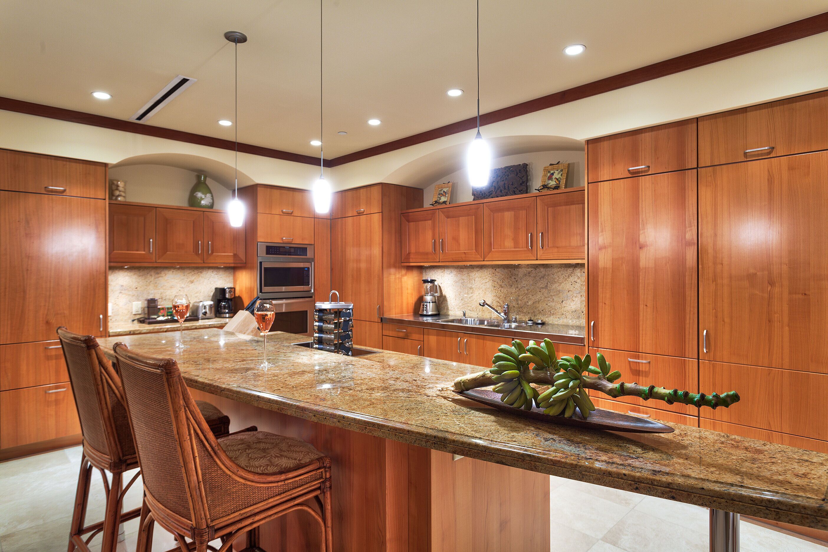 A kitchen with wooden cabinets, a granite countertop, and a bar area with wicker chairs.