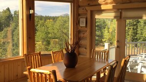 A wooden cabin interior with a dining table and chairs, a chandelier, and framed pictures on the walls.