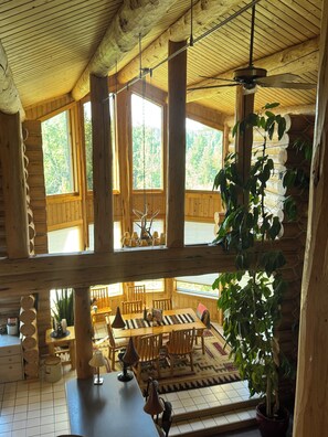 Een ruime hut met hoge plafonds, grote ramen en een eethoek met houten meubels.