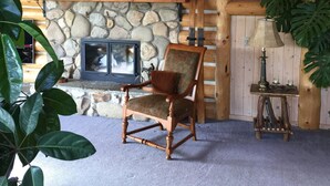 A cozy log cabin interior with a stone fireplace, a wooden chair, and a ladder leading to a loft area.