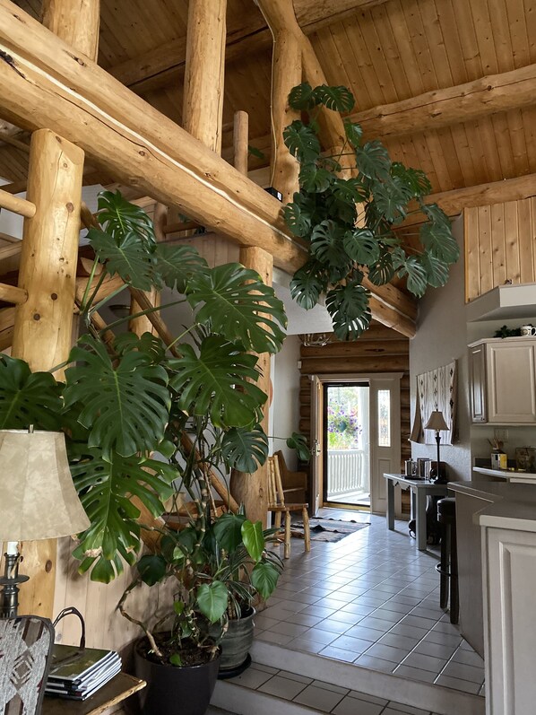 A spacious kitchen with wooden beams, a dining area, and large potted plants.