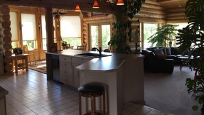 A spacious living area with a kitchen island, wooden furniture, and large windows allowing natural light.
