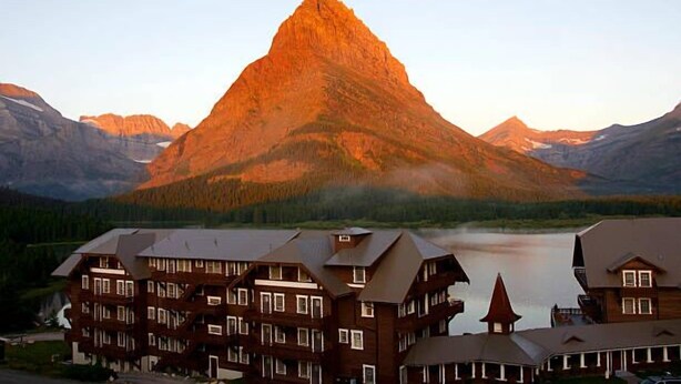 A mountain lodge with multiple buildings, a lake, and a prominent mountain peak in the background.