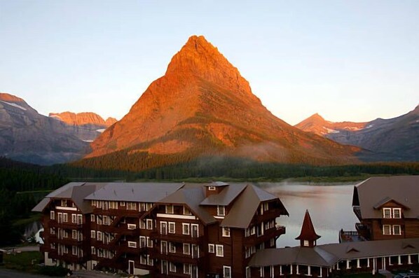 Un chalet de montagne composé de plusieurs bâtiments, avec un lac et un sommet montagneux imposant en arrière-plan.