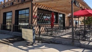 Un edificio con pérgola de madera, asientos exteriores y un letrero que dice 'OPEN'.