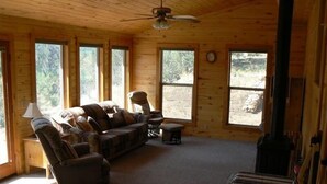 Un acogedor interior de cabaña con un sofá, sillones, una mesita y una chimenea.