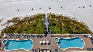 An aerial view of a beach resort with two swimming pools, beach umbrellas, and lounge chairs.