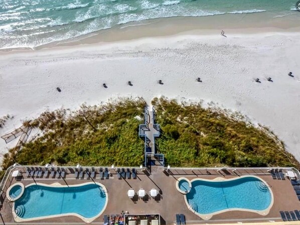 An aerial view of a beach resort with two swimming pools, beach umbrellas, and lounge chairs.