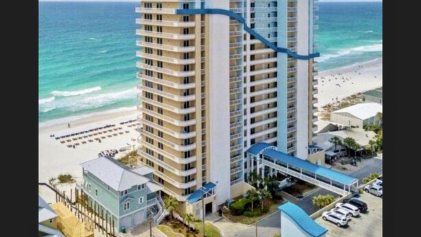 A high-rise hotel with multiple balconies, a beach view, and a parking area.