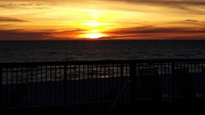A sunset over the ocean with a wooden railing in the foreground.