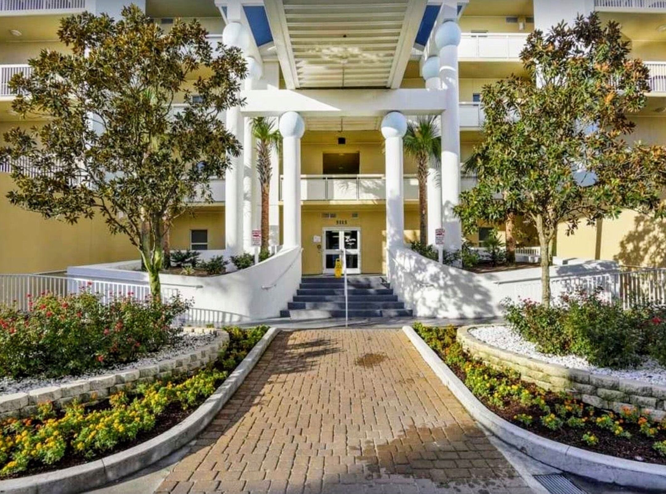 A hotel entrance with a central staircase, white columns, and a yellow facade.
