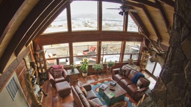 Ein gemütliches Wohnzimmer mit Holzboden, einem Steincheminée und einem großen Fenster mit Blick auf einen Balkon.