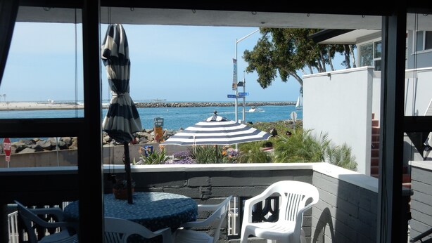 Een terras met een tafel en stoelen, een gestreept parasol en uitzicht op zee en de pier.