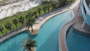 Una piscina de diseño curvo, rodeada de palmeras y sillones de descanso.