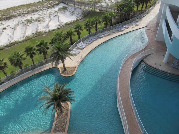 A pool with a curved design, surrounded by palm trees and lounge chairs.