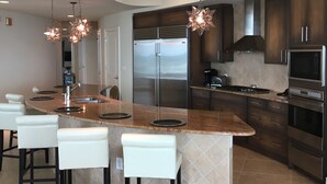 Una cocina moderna con una isla central, taburetes de bar, electrodomésticos de acero inoxidable e iluminación colgante.