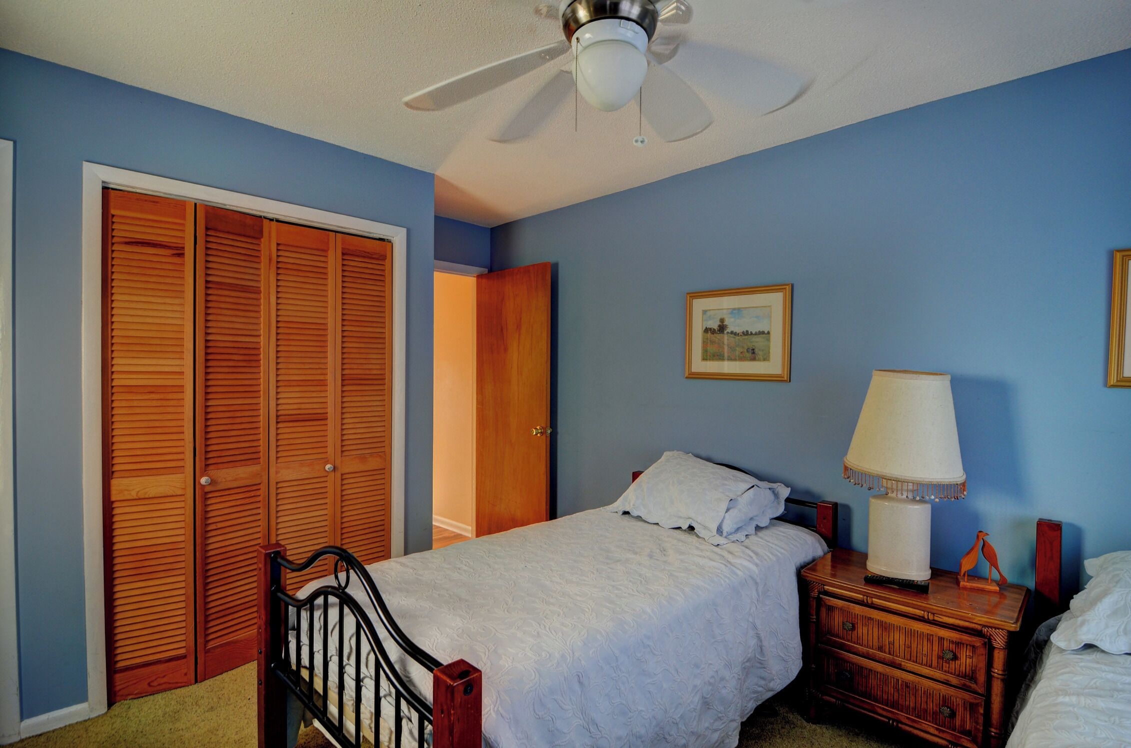 A bedroom with a bed, nightstand, wooden closet, and a ceiling fan.