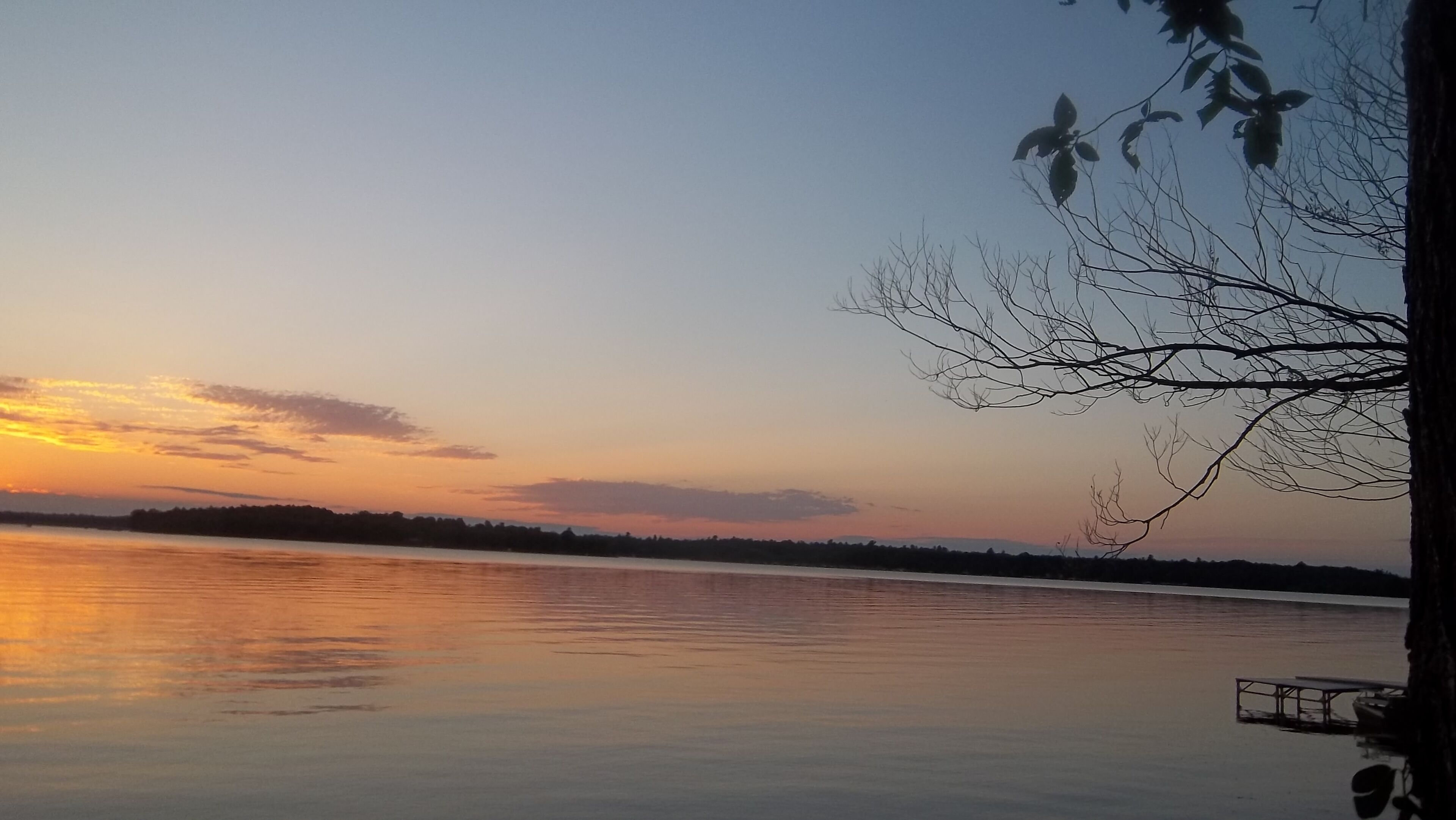 Ein ruhiger See bei Sonnenuntergang mit einem Steg und einem Boot.