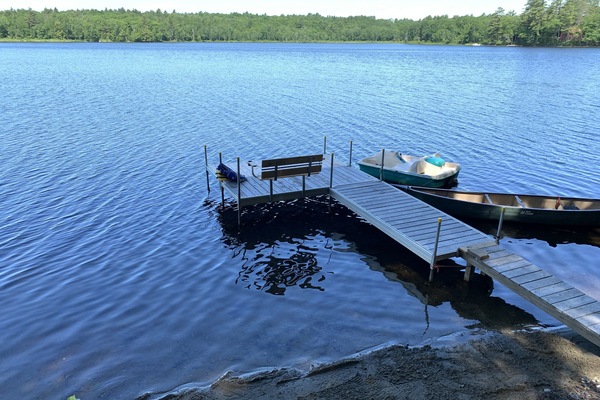 Beach area and dock complete with dock bench, canoe, and paddle boat.