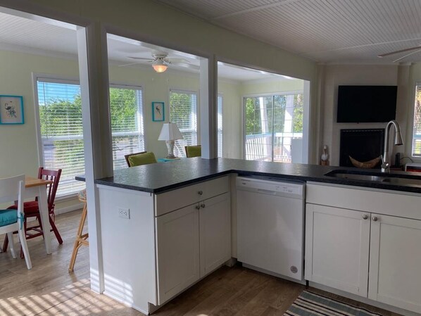 A kitchen with white cabinets, a dishwasher, a black countertop, and a ceiling fan. There is a dining area with a table and chairs, and a view of a deck with a railing.