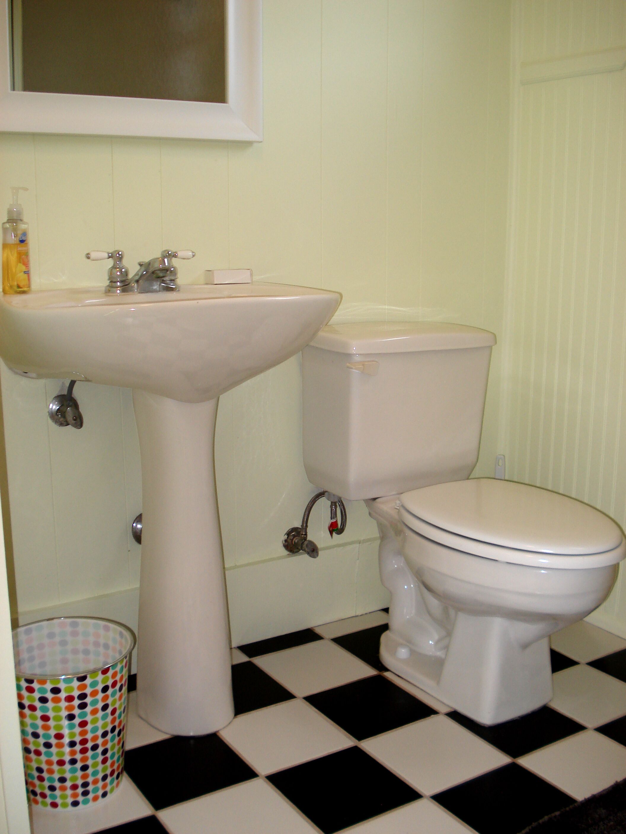 Un baño con lavamanos blanco, inodoro y cubo de basura con tapa de colores.