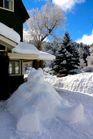 Un paysage enneigé avec une maison et un grand bonhomme de neige devant.
