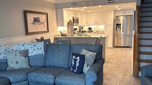 A modern living room with a sofa, coffee table, and a kitchen area in the background. - Gulf-Front - steps to the beach - 3 bed/3 bath = Free Parking (Orange Beach)