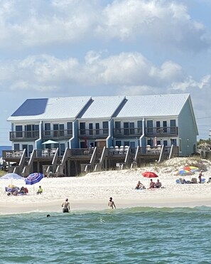 En bygning ved stranden med flere balkoner og en sandstrand i forgrunden.