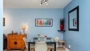 Un comedor con una mesa de vidrio, sillas blancas, un armario de madera y un cuadro abstracto de colores en la pared.