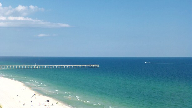 A beach with a pier extending into the ocean, clear skies, and calm waters.