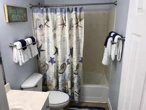 Baño con cortina de ducha adornada con criaturas marinas, inodoro, bañera y toallas colgadas en barras.
