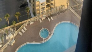 A view of a hotel with a pool, a beach, and a parking area.