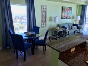 Un comedor con una mesa y sillas de vidrio, un sofá con cojines a rayas, y vistas al exterior.