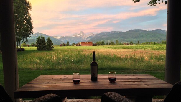 Ein Holztisch mit zwei Gläsern und einer Weinflasche, vor einer malerischen Berglandschaft.