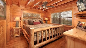 A log cabin bedroom with a wooden bed, two bedside lamps, a ceiling fan, and a window with blinds. - Mountain Splendor: Best Mountain View in Starr Crest Resort - Brand New Hot Tub (Sevierville)